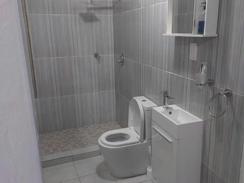 A modern, compact bathroom featuring floor-to-ceiling grey tiled walls, a walk-in shower with a rain shower head, and a wall-mounted vanity unit.