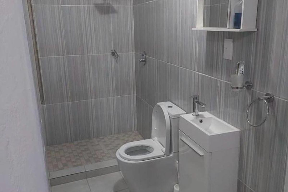 A modern, compact bathroom featuring floor-to-ceiling grey tiled walls, a walk-in shower with a rain shower head, and a wall-mounted vanity unit.