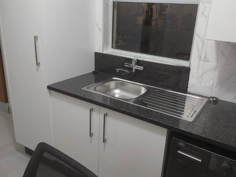 A functional laundry area featuring modern white cabinetry, a dark granite countertop, and a stainless steel sink with a window view.