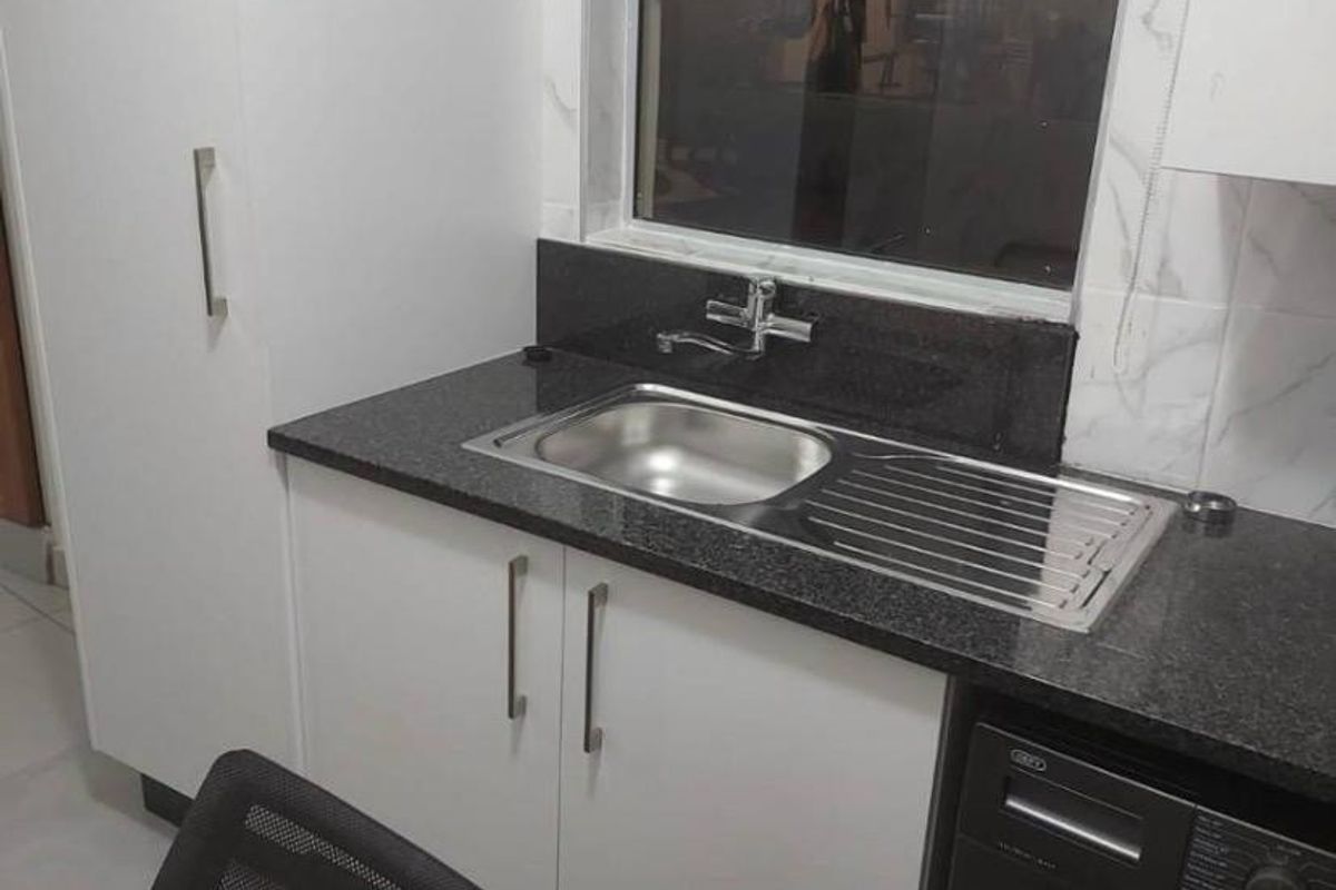 A functional laundry area featuring modern white cabinetry, a dark granite countertop, and a stainless steel sink with a window view.