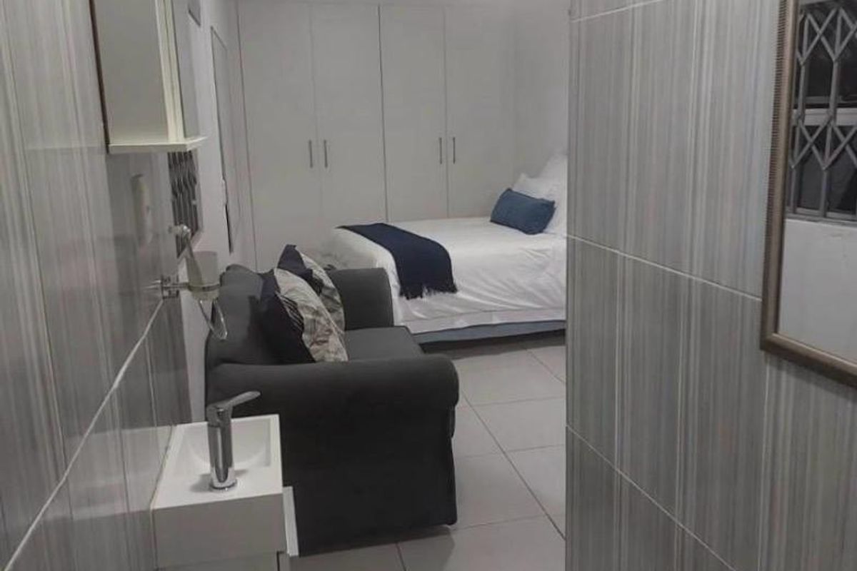 A bedroom featuring tiled flooring, built-in cupboards, and an integrated en-suite bathroom area with a wall-mounted basin and toilet.