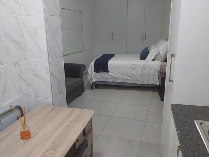 Open-plan studio living space featuring tiled flooring, built-in cupboards, and a compact kitchen area with modern marble-look wall tiling.