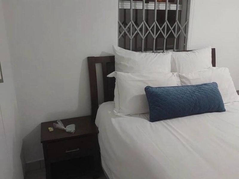 A functional bedroom featuring tiled flooring, a window with a security gate, and a roller blind.