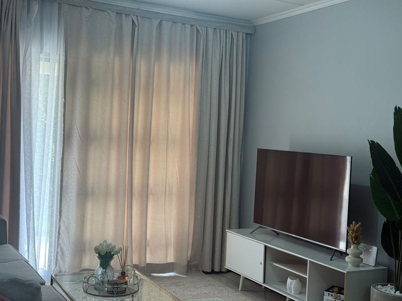 A well-lit living room featuring a large sliding glass door with floor-to-ceiling curtains and decorative crown molding.