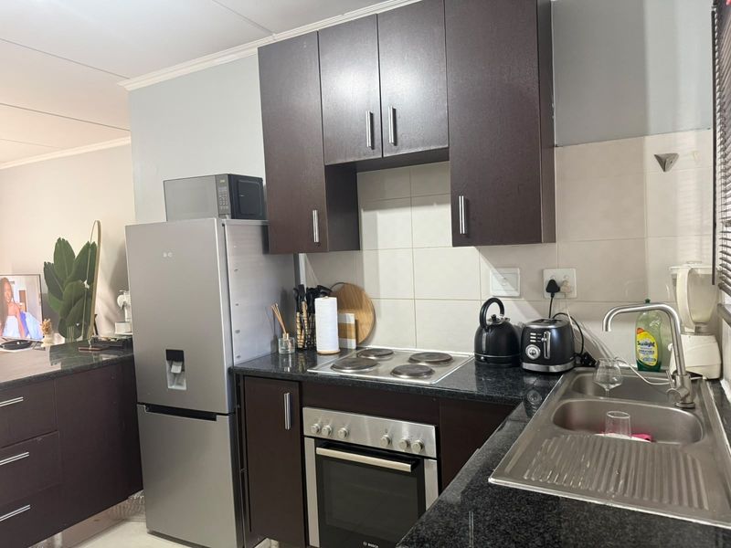 A functional kitchen featuring dark wood cabinetry, granite countertops, a stainless steel sink, and built-in oven with electric hob.