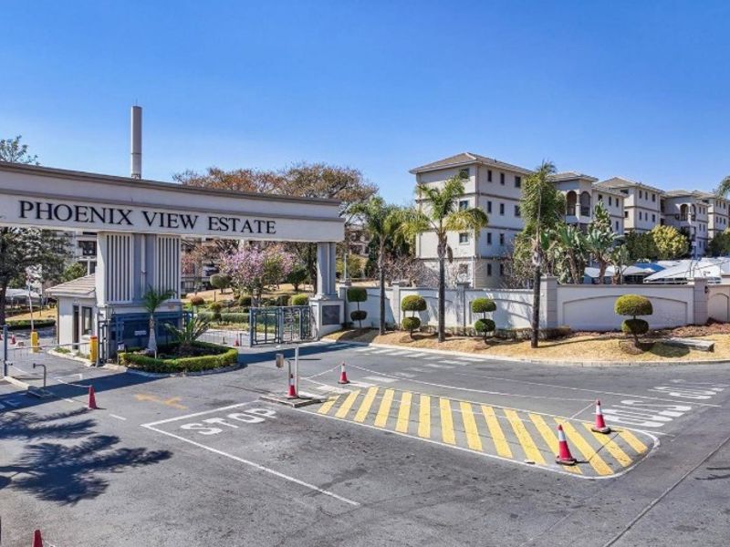 The main entrance and security gatehouse of Phoenix View Estate, featuring a paved driveway, perimeter walling, and well-maintained landscaped grounds.