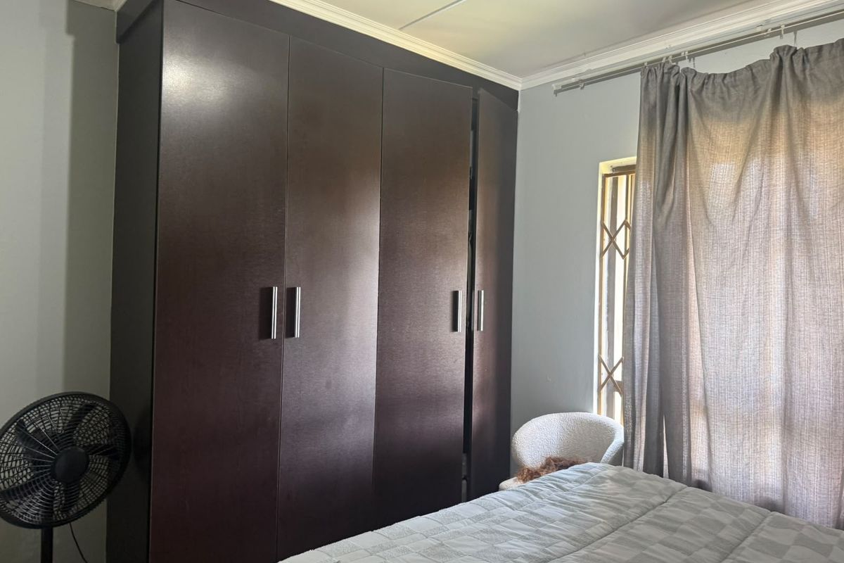 A bedroom featuring a large dark wood built-in wardrobe and a window fitted with a security gate.