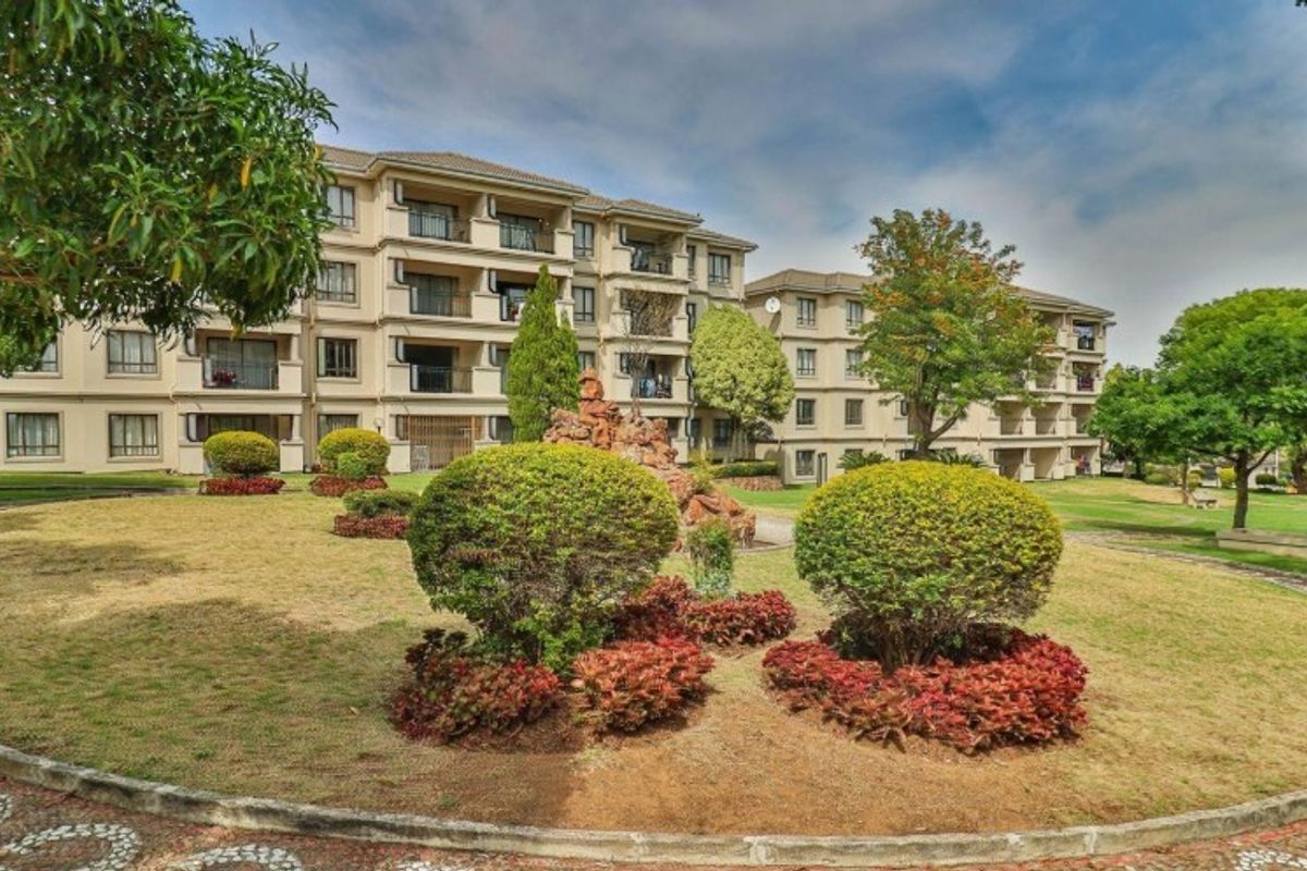 A view of the apartment complex exterior featuring a well-maintained landscaped garden, paved walkways, and multiple residential balconies.