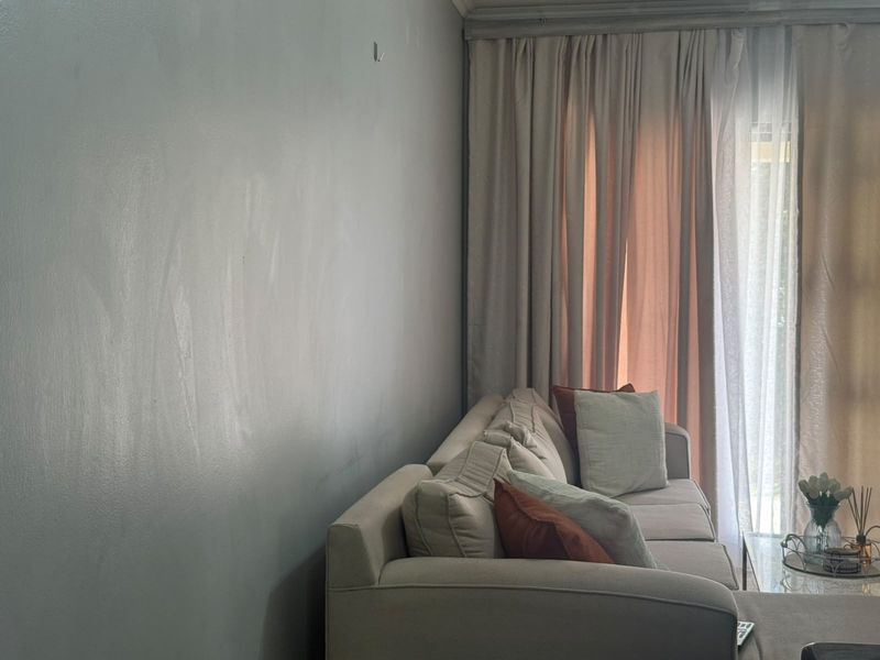 A living room area featuring a large sliding glass door with floor-to-ceiling curtains and a plain wall finish.