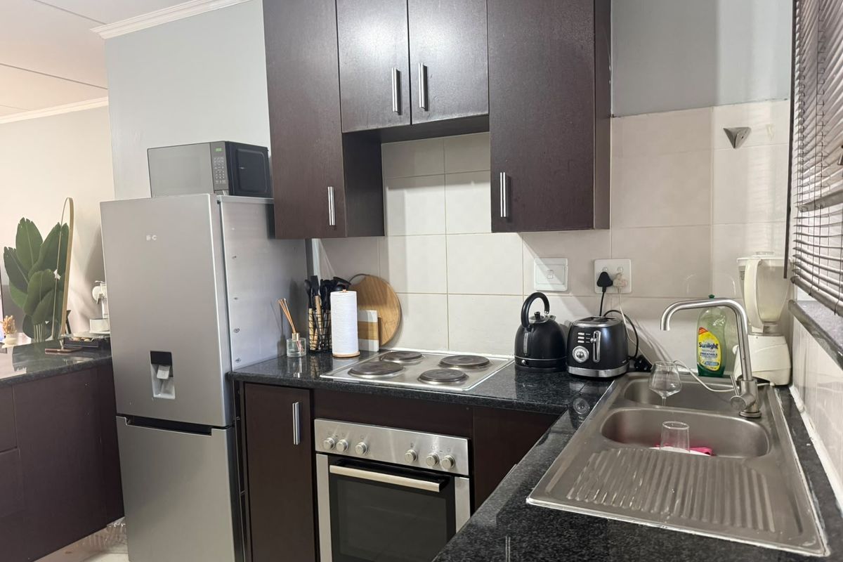 A functional kitchen featuring dark wood cabinetry, granite countertops, a stainless steel sink, and built-in electric oven and hob.