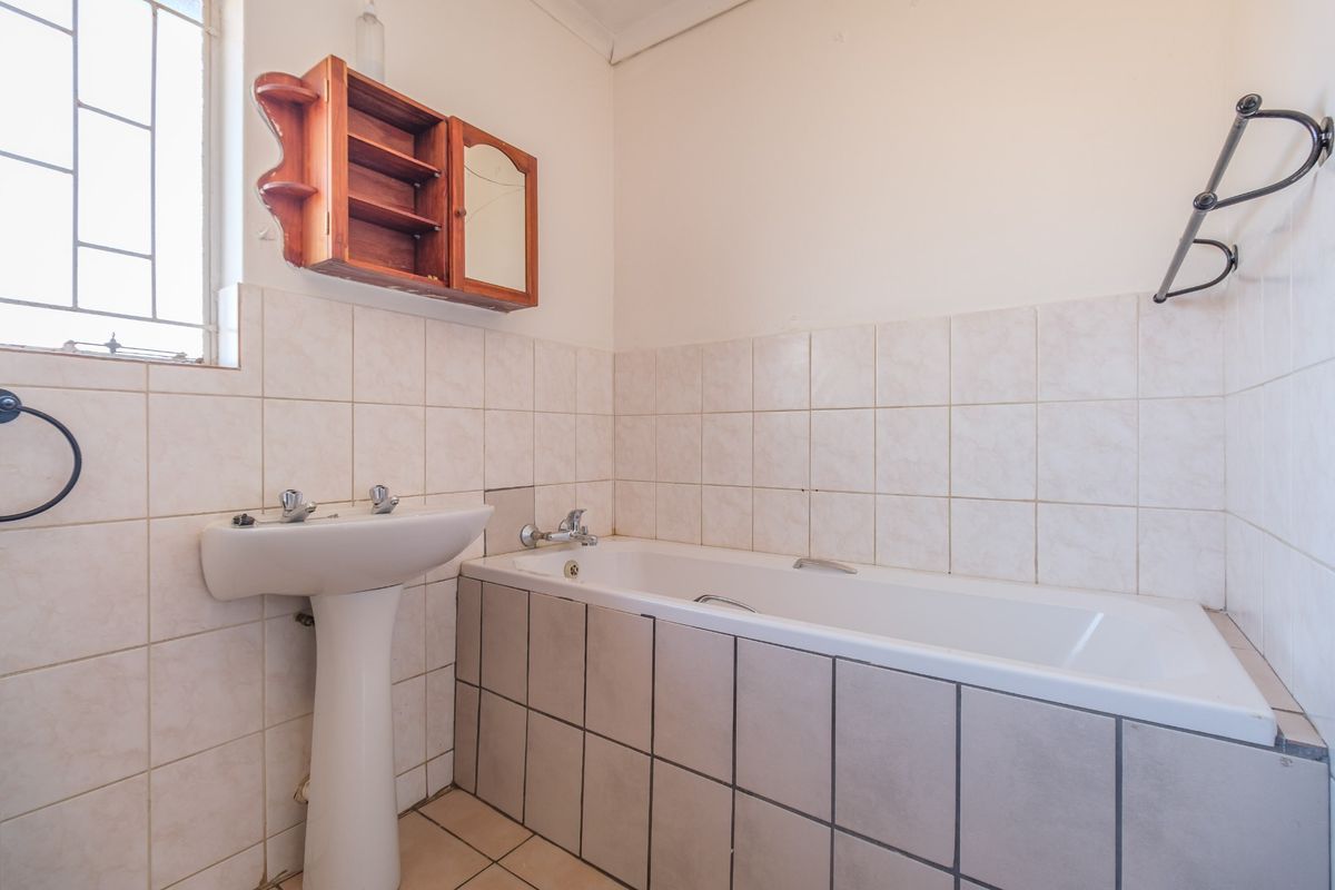A functional bathroom featuring a pedestal basin, bathtub, and neutral wall tiling, offering a clean canvas for potential modern updates.