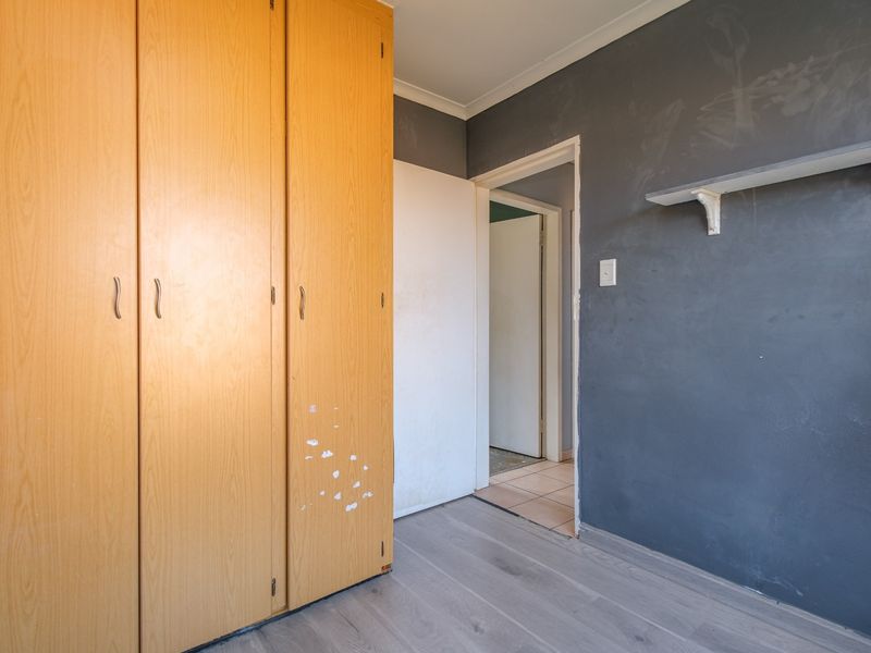 An empty bedroom featuring laminate flooring, built-in wooden cupboards, and a dark accent wall with a mounted shelf.