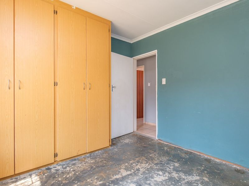 An empty bedroom featuring built-in wooden cupboards and teal-painted walls, requiring flooring replacement and general cosmetic refurbishment.