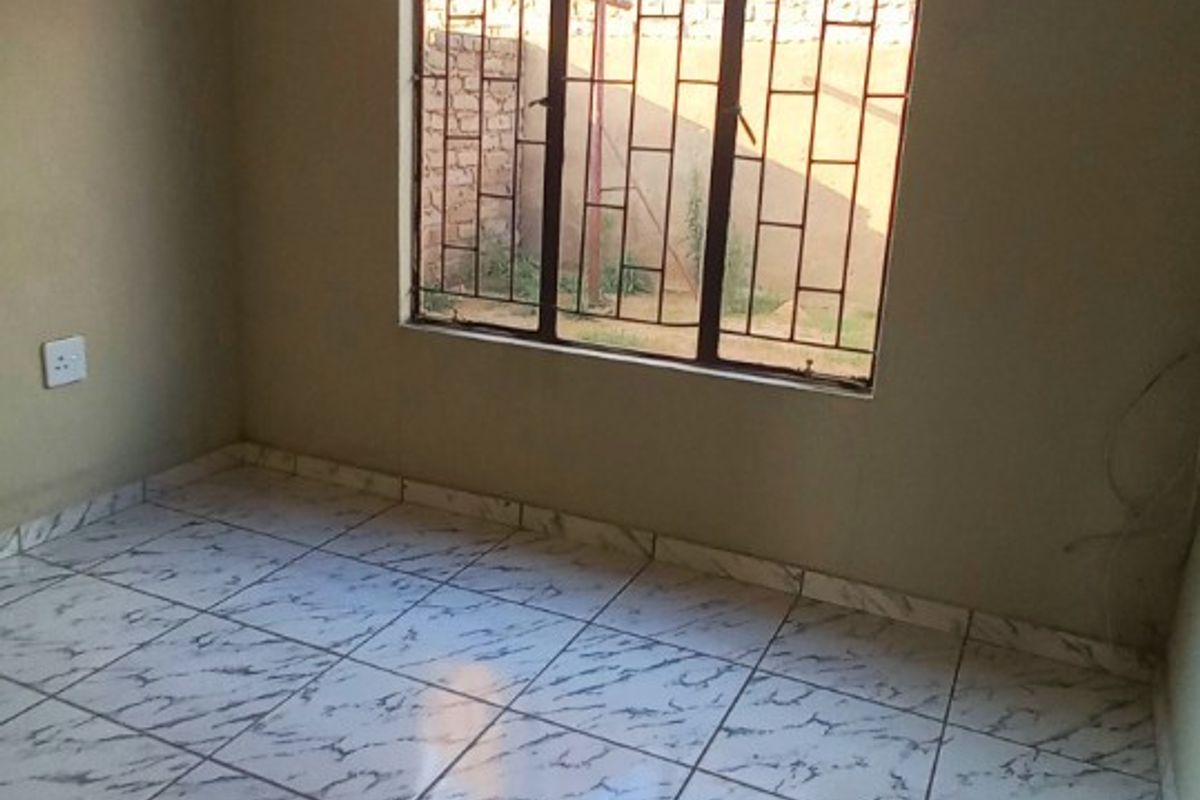 An empty bedroom featuring tiled flooring and a window fitted with security bars.