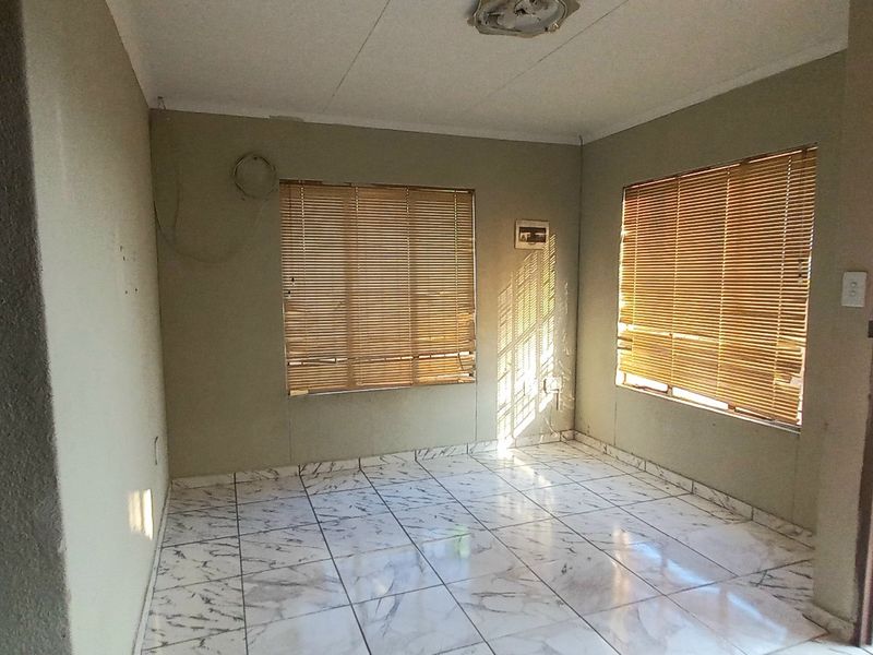 An empty living room featuring tiled flooring, venetian blinds, and a ceiling light fixture, with some minor wall imperfections.