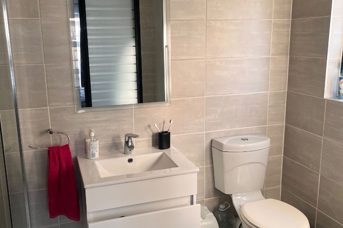 A modern bathroom featuring a wall-mounted vanity, ceramic basin, toilet, and full-height wall tiling with a glass shower enclosure.