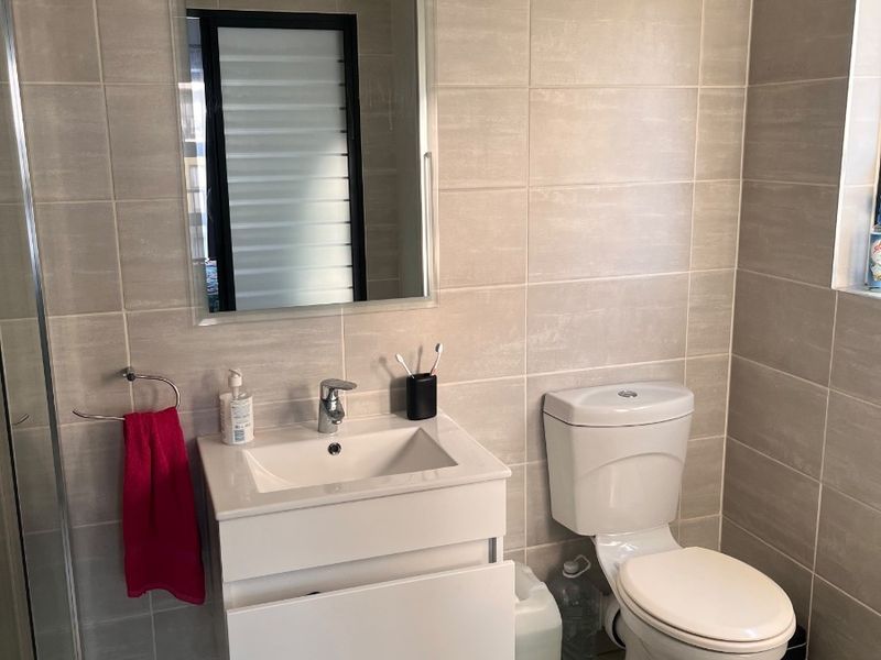 A modern bathroom featuring a wall-mounted vanity, ceramic basin, toilet, and full-height wall tiling with a glass shower enclosure.