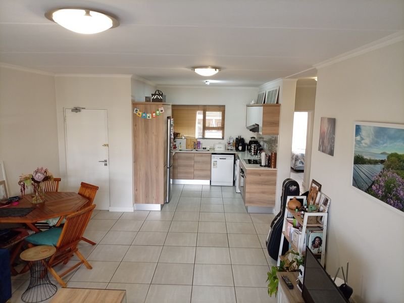 Open-plan living and kitchen area featuring modern wood-finish cabinetry, tiled flooring, and functional built-in appliances in a well-maintained apartment setting.