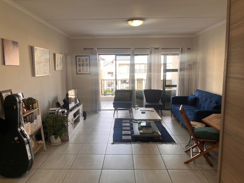 A bright living room featuring tiled flooring and large sliding glass doors that open onto a private balcony, providing ample natural light.