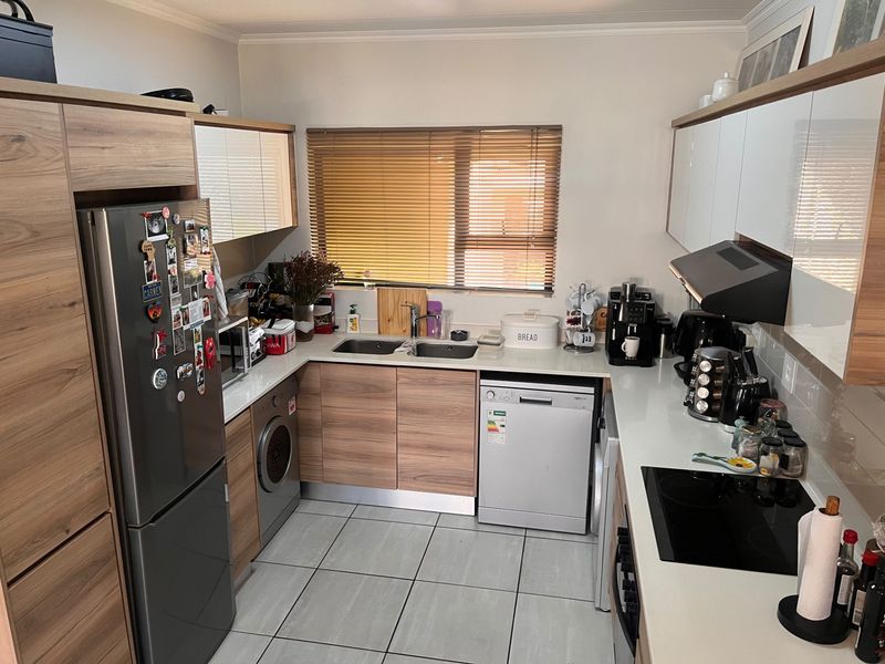 A well-maintained kitchen featuring modern wood-finish cabinetry, stone-look countertops, a double sink, integrated hob, and extractor fan with tiled flooring.