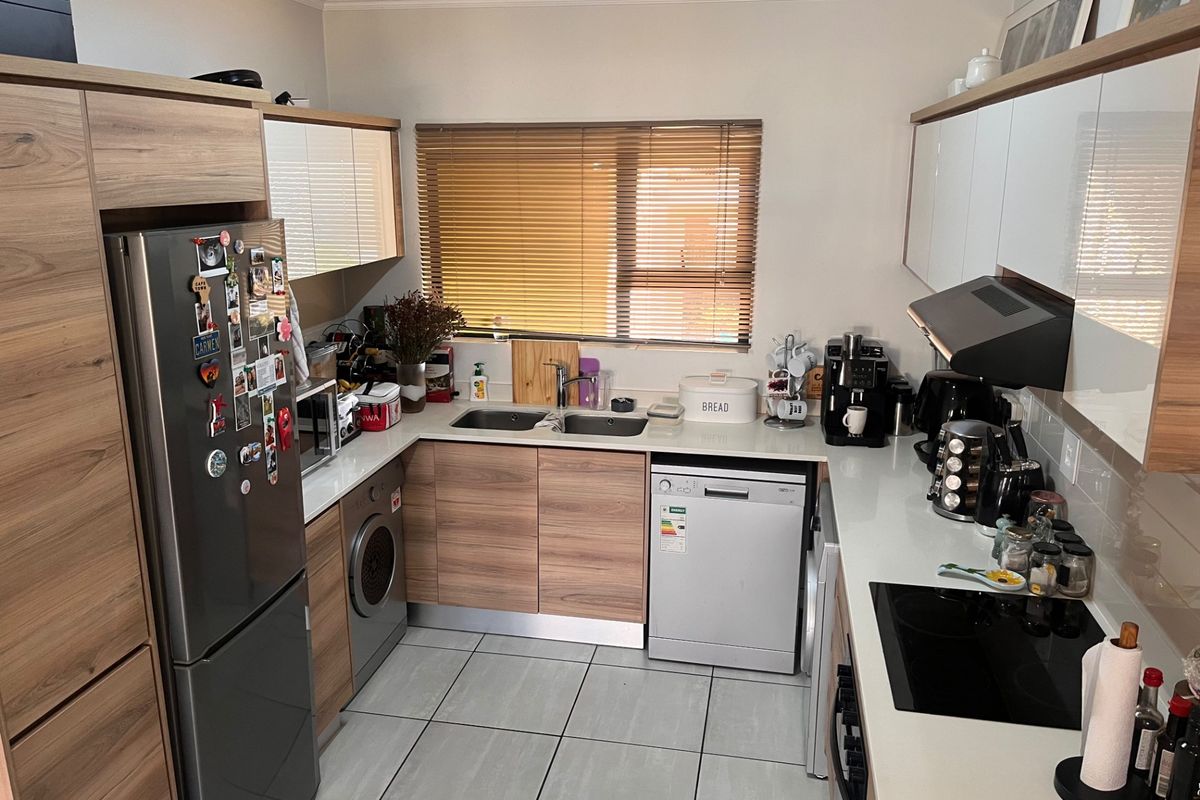 A well-maintained kitchen featuring modern wood-finish cabinetry, stone-look countertops, a double sink, integrated hob, and extractor fan with tiled flooring.