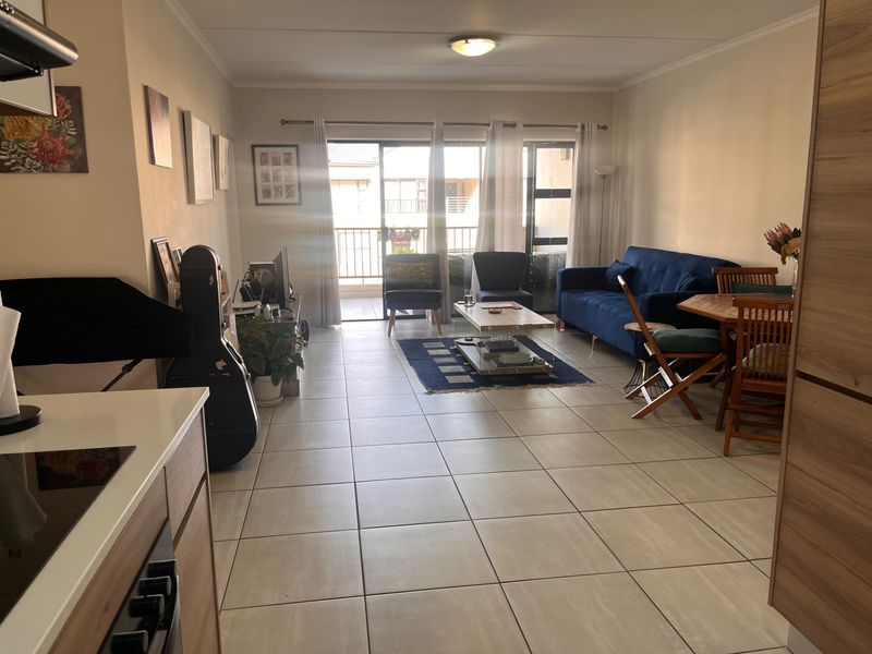 Open-plan living and kitchen area featuring neutral ceramic floor tiles, modern cabinetry, and direct access to a private balcony through sliding glass doors.