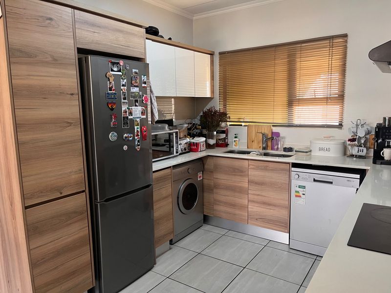 A functional kitchen featuring modern wood-look cabinetry, tiled flooring, stainless steel sink, and integrated appliances including an oven and extractor fan.