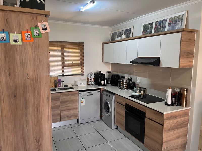 Modern kitchen featuring wood-grain cabinetry, white countertops, integrated appliances including an oven, hob, and dishwasher, with tiled flooring and natural light.