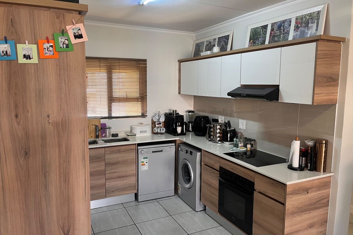 Modern kitchen featuring wood-grain cabinetry, white countertops, integrated appliances including an oven, hob, and dishwasher, with tiled flooring and natural light.