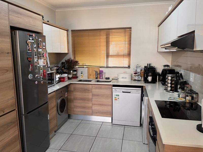 A well-maintained kitchen featuring modern wood-grain cabinetry, stone countertops, integrated appliances, and tiled flooring with a functional U-shaped layout.