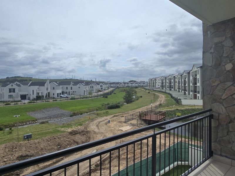 A covered balcony featuring stone wall cladding and a metal balustrade, offering an elevated view over the surrounding residential estate and landscape.