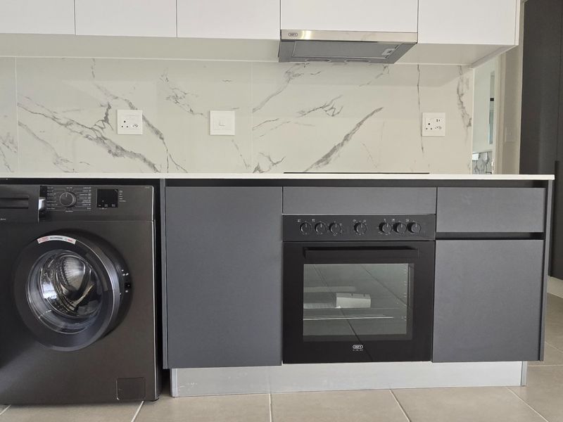 Modern kitchen featuring sleek dark grey cabinetry, white marble-look splashback, built-in oven, extractor fan, and stone countertops in a clean, contemporary space.