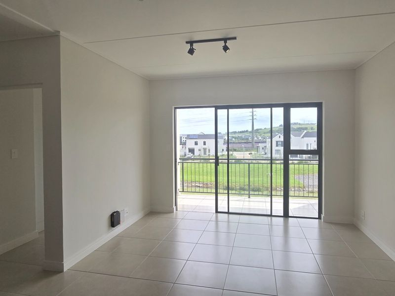 Bright open-plan living area featuring neutral tiled flooring, modern track lighting, and large sliding glass doors leading to a private balcony.
