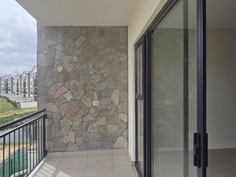 A covered balcony featuring stone cladding, tiled flooring, and a metal balustrade, offering views over the surrounding estate.