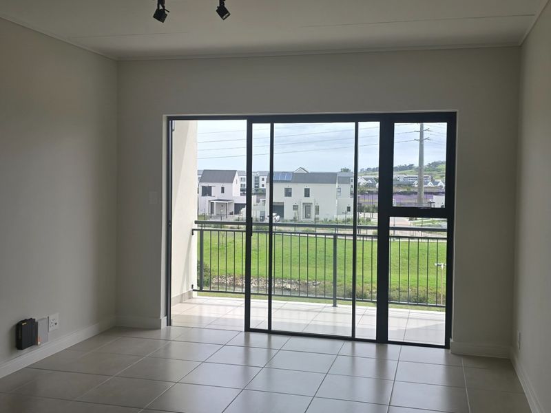 An empty, well-maintained living area featuring neutral tiled flooring and a large sliding glass door that opens onto a private balcony.