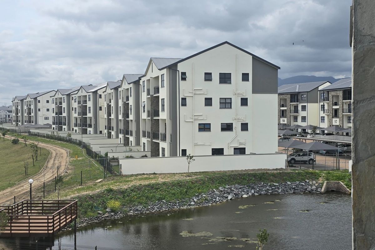 View of the apartment complex exterior featuring multi-story residential blocks, landscaped grounds, a small pond, and dedicated carport parking areas.