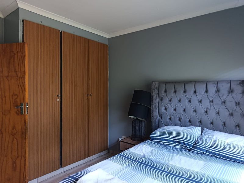 A bedroom featuring built-in wooden cupboards, grey painted walls, and tiled flooring.