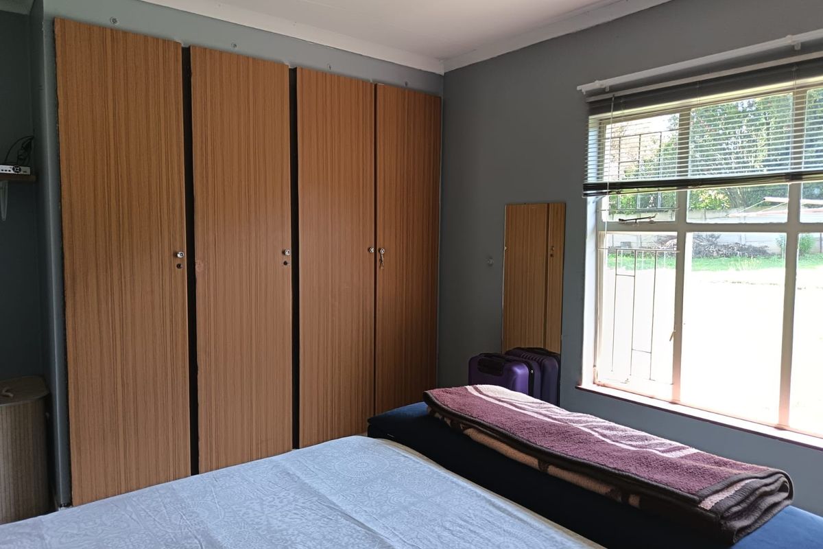 A bedroom featuring built-in wooden cupboards, a window with security bars, and venetian blinds, offering a functional and well-lit living space.