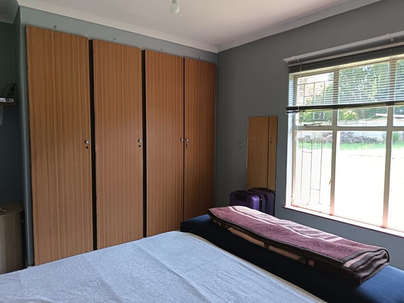 A bedroom featuring built-in wooden cupboards, a window with security bars, and venetian blinds, offering a functional and well-lit living space.
