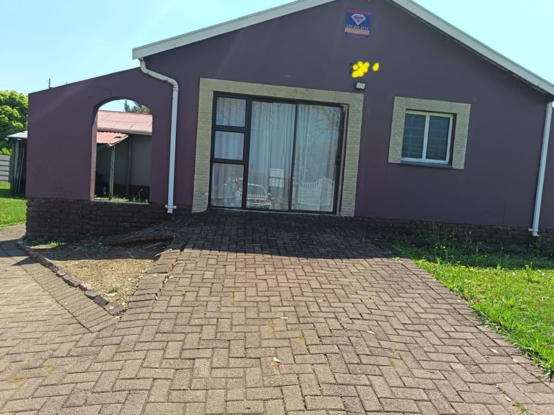 Rear exterior view of the property featuring a paved walkway leading to a sliding glass door entrance with brick facade and guttering.