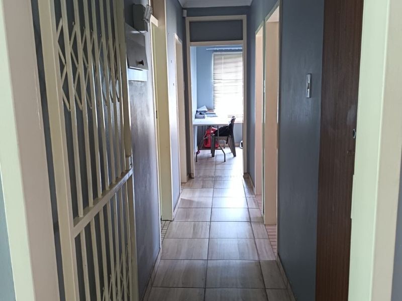 A functional hallway featuring tiled flooring, a security gate, and a ceiling access hatch, providing access to various rooms within the home.