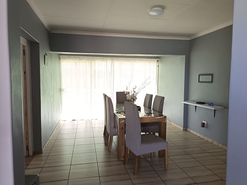 A dining room featuring tiled flooring, a wall-mounted shelf, and a sliding glass door that provides natural light.
