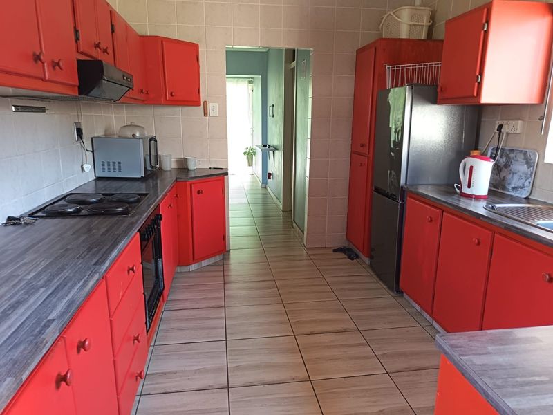 A functional kitchen featuring bright red cabinetry, dark laminate countertops, tiled flooring, and a built-in electric hob with an extractor fan.