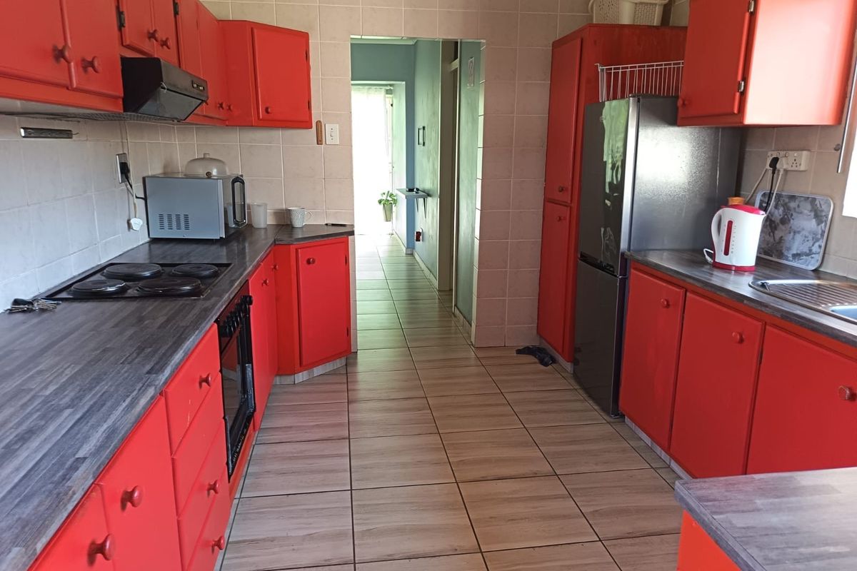 A functional kitchen featuring bright red cabinetry, dark laminate countertops, tiled flooring, and a built-in electric hob with an extractor fan.