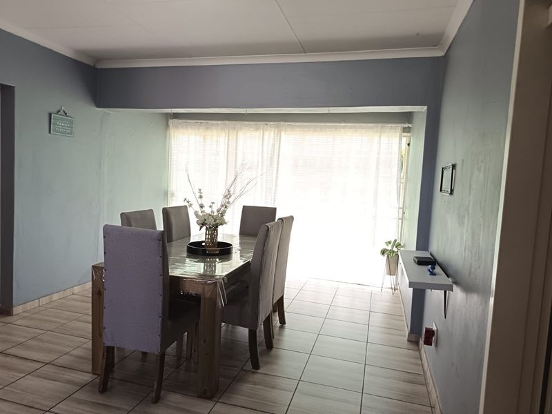 A dining room featuring tiled flooring, neutral wall tones, and a wall-mounted shelf, providing a functional space for family meals.