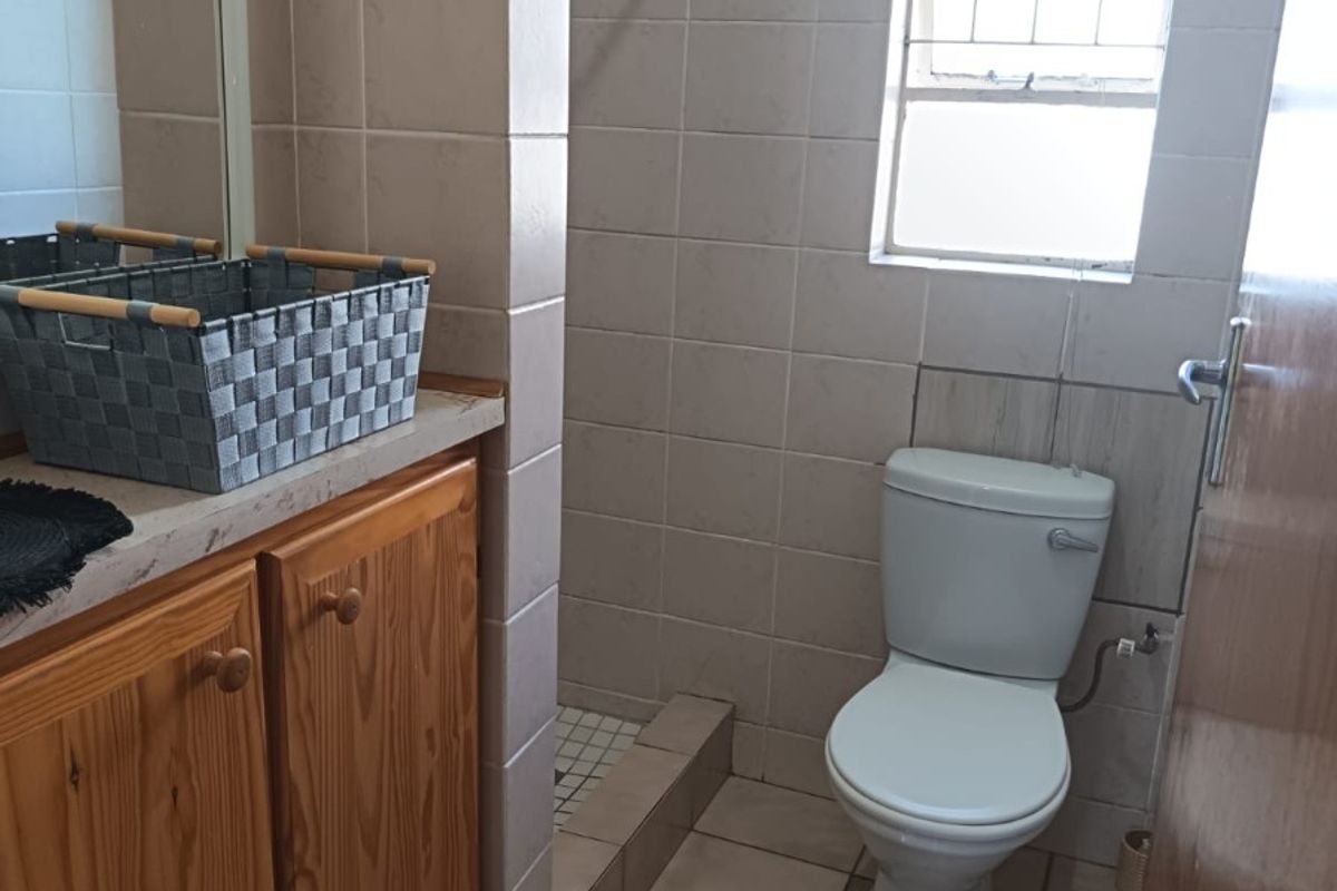 A functional bathroom featuring a vanity cabinet, toilet, and a tiled shower area with a window for natural light.