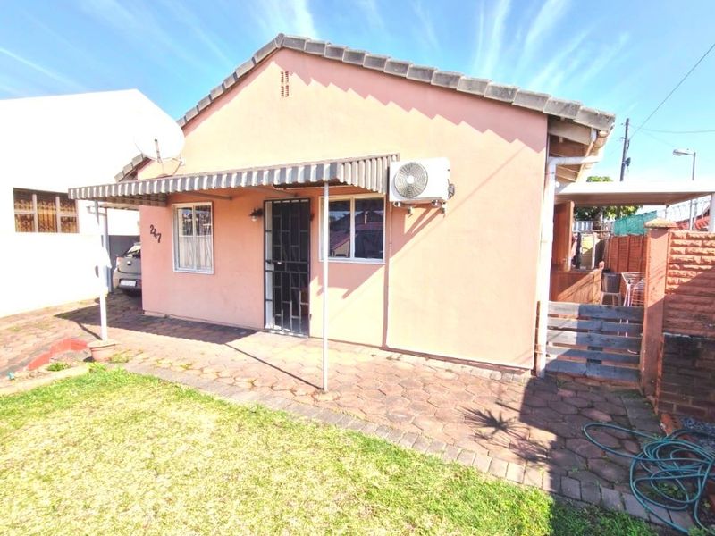 Rear exterior view of a single-story house featuring a paved patio area, metal awning, and a small garden space.