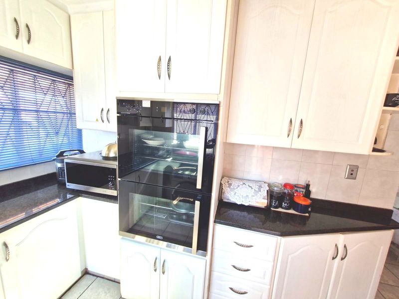 A functional kitchen featuring white cabinetry, dark granite countertops, a built-in double oven, and a tiled backsplash.