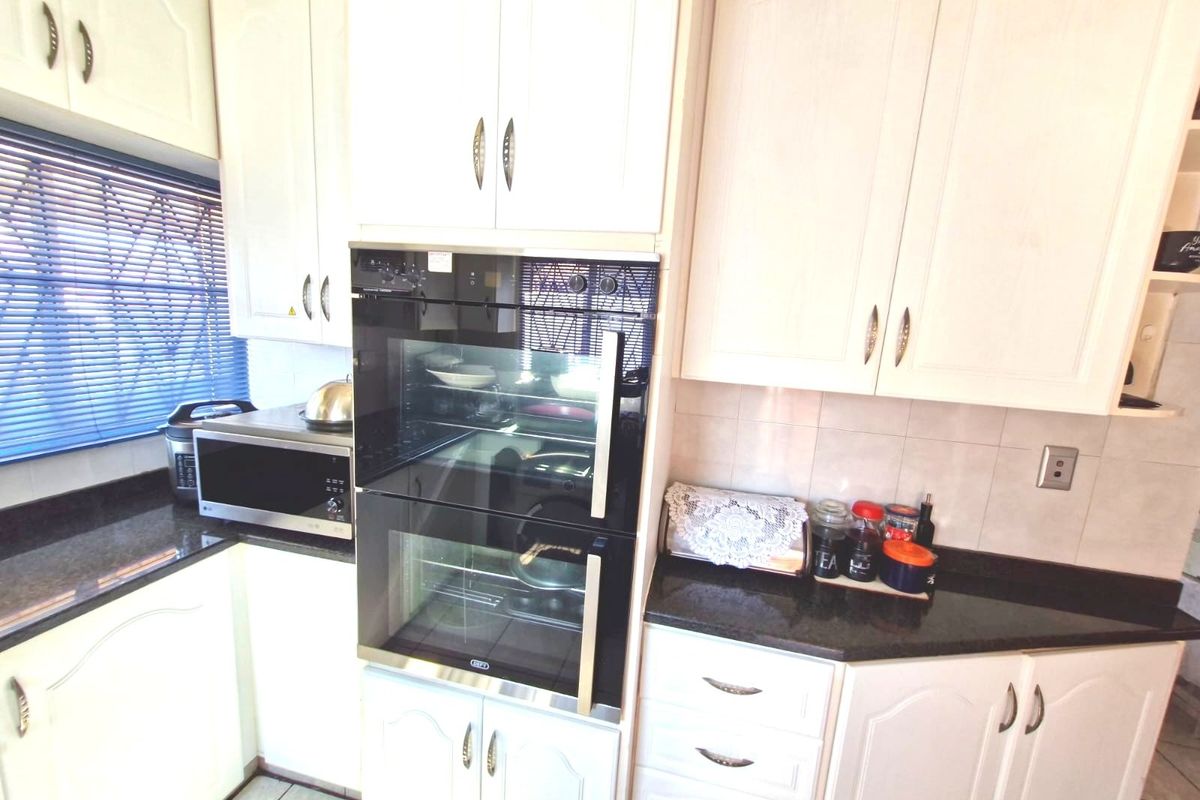 A functional kitchen featuring white cabinetry, dark granite countertops, a built-in double oven, and a tiled backsplash.