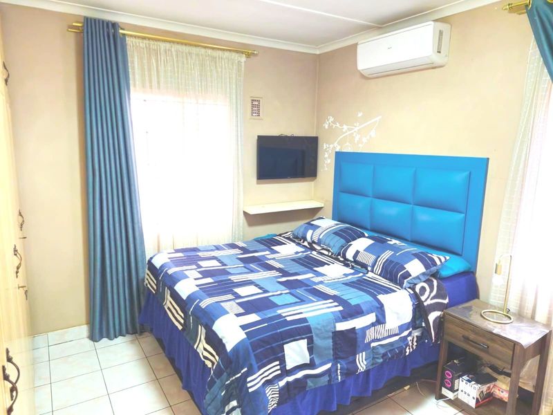 A functional bedroom featuring tiled flooring, a wall-mounted air conditioning unit, and built-in shelving, providing a comfortable and practical living space.